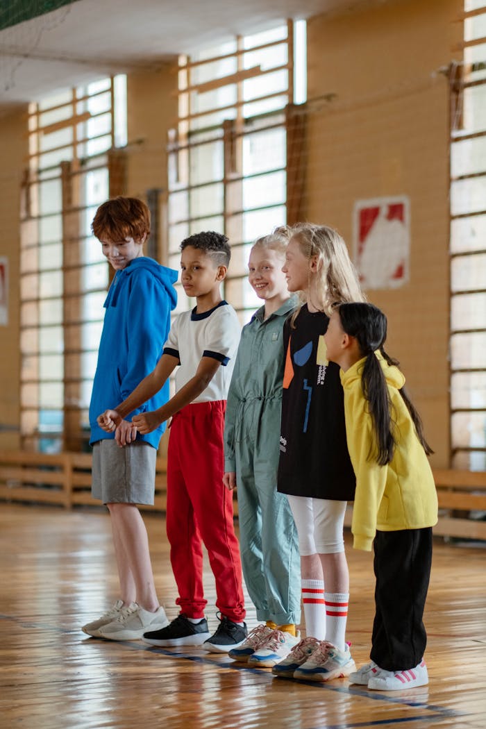 A diverse group of children lined up in a school gym, ready for a sport activity.