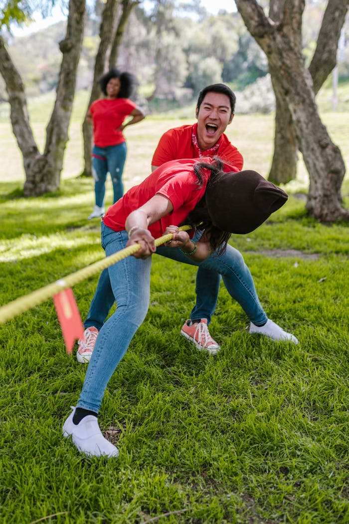 Group of adults engaged in a lively tug of war game in a park setting.